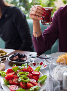 Mujer disfrutando de un té con platos de comida saludable, representando el enfoque en bienestar físico y metabólico a través de la nutrición y hábitos saludables.